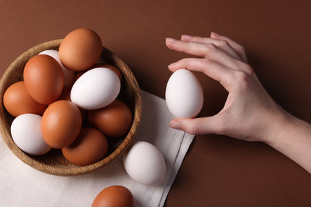 Woman with raw eggs on brown background, closeupの写真素材