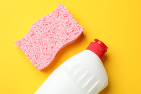Pink sponge and dish soap on yellow background, flat layの写真素材