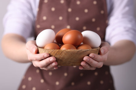 Woman with bowl of raw eggs on grey background, closeupの写真素材