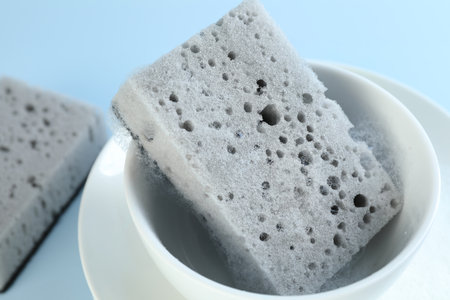 Sponge with foam and dishware on light blue background, closeupの写真素材