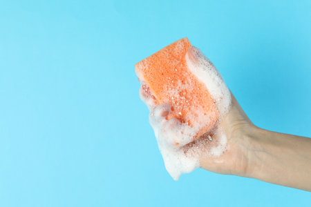 Woman holding sponge with foam on light blue background, closeup. Space for textの写真素材