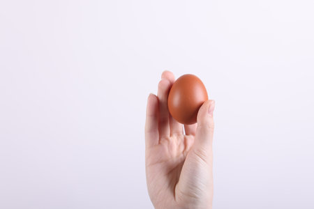 Woman holding raw egg on light background, closeup. Space for textの写真素材