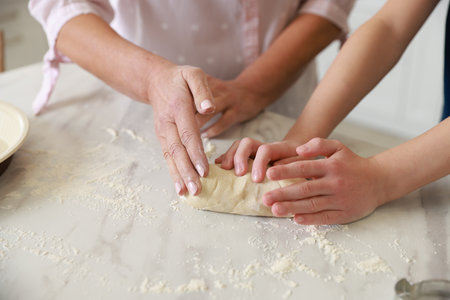 Grandmother and her grandson kneading dough at white marble table in kitchen, closeupの写真素材