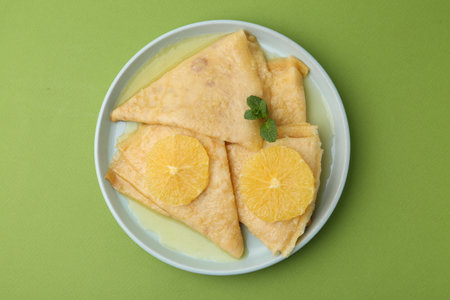 Delicious Crepes Suzette on green background, top view
