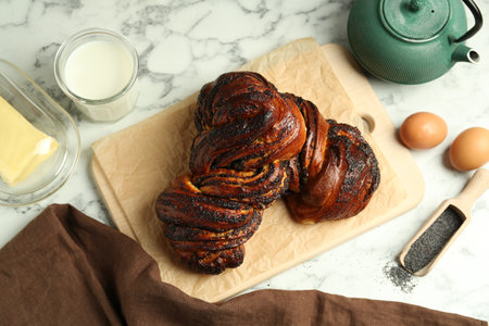 Tasty buns with poppy seeds and products on white marble table, flat lay