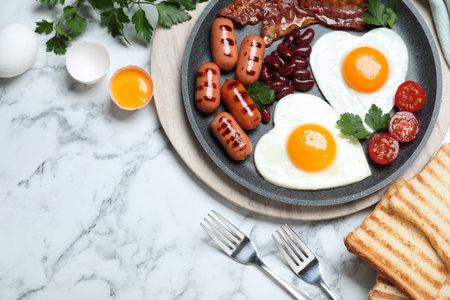 Delicious breakfast with heart shaped fried eggs and sausages served on white marble table, flat layの写真素材