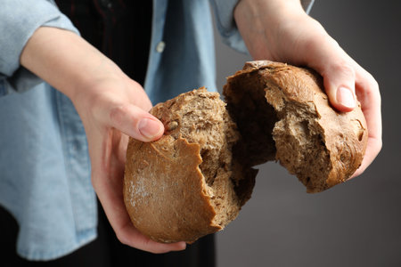 Woman breaking loaf of fresh rye bread on grey background, closeupの写真素材