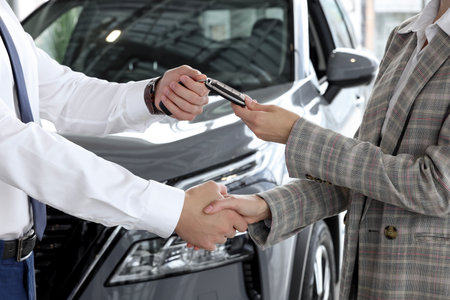 Salesman giving key to client near new car in salon, closeupの写真素材