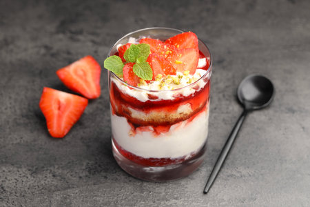 Tasty trifle dessert. Strawberries, sponge cake and whipped cream in glass on grey tableの写真素材