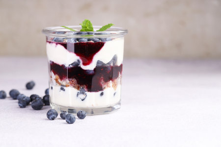 Tasty trifle dessert. Blueberries, sponge cake and whipped cream in glass on light grey table, space for textの写真素材