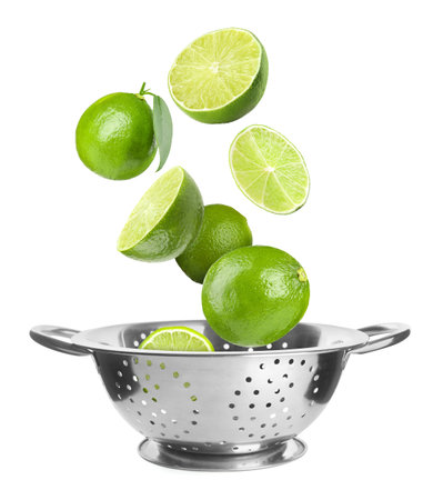 Fresh limes falling into colander on white backgroundの写真素材