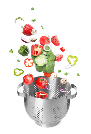 Different fresh vegetables falling into colander on white background