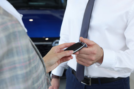 Saleswoman giving key to client near new car in salon, closeup