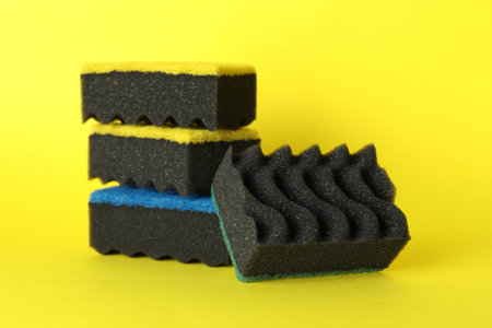 Different clean sponges on yellow background, closeup