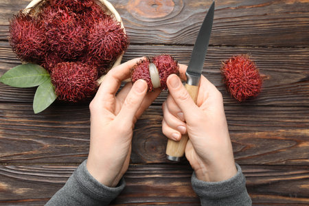 Woman peeling ripe rambutan at wooden table, top viewの写真素材
