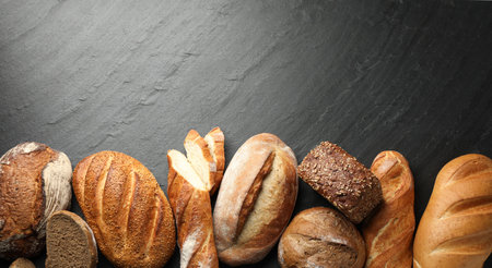 Loafs of different bread on black background, flat lay. Space for text