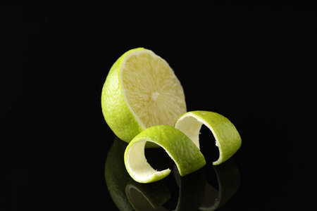 Lime peel and half of fresh fruit on black mirror surface, closeup