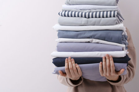 Woman holding stack of clean bed lines on light gray background