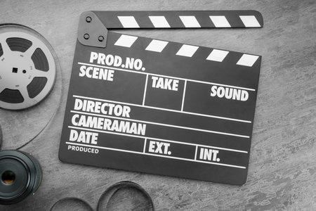 Flat lay composition with movie clapper, film reel and camera lens on gray textured tableの写真素材