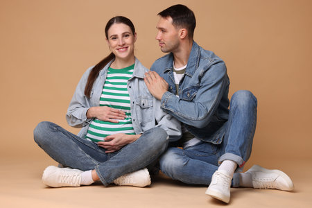 Pregnant woman and her husband on beige backgroundの写真素材