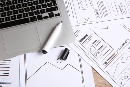 Developing UI design. Sketches of website wireframes, laptop and felt pen on wooden table, above...