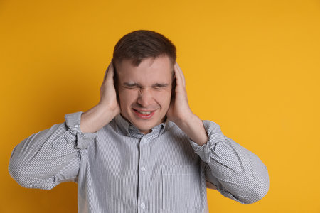 Man covering his ears on orange backgroundの写真素材