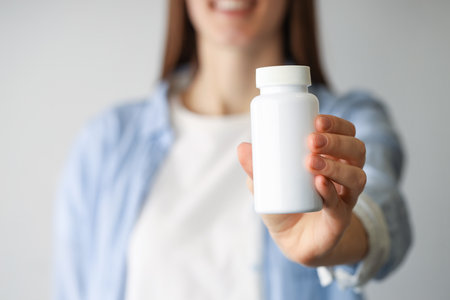 Woman holding medical bottle with pills on light background, closeupの写真素材