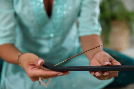 Young woman with incense stick smoldering in holder indoors, closeupの写真素材