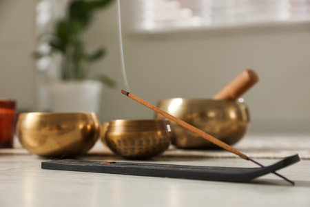 Incense stick smoldering in holder and tibetan singing bowls on floor, selective focusの写真素材
