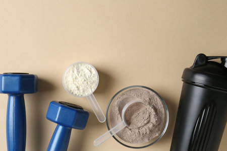Protein powder, shaker and dumbbells on beige background, flat lay. Space for textの写真素材