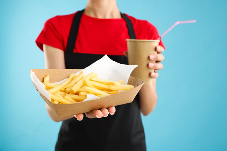 Fast-food worker with paper cup and fries on light blue background, closeupの写真素材