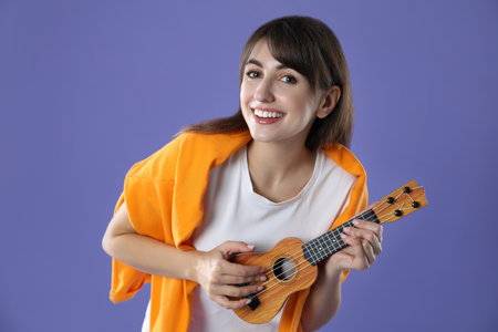 Happy woman playing ukulele on purple background