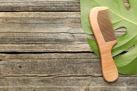 Comb and monstera leaf on wooden table, top view. Space for text