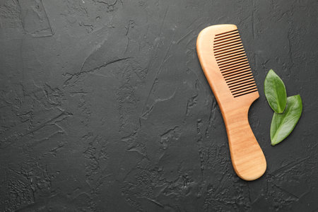 Wooden comb and leaves on dark textured table, flat lay. Space for textの写真素材