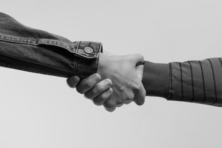 Help and support. People holding hands on light grey background, closeup. Toned in black and white