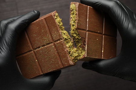 Person breaking chocolate bar with pistachio and knafeh at dark table, closeup