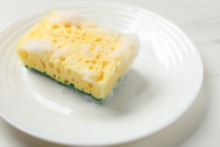 Yellow sponge with foam and plate on white table, closeupの写真素材