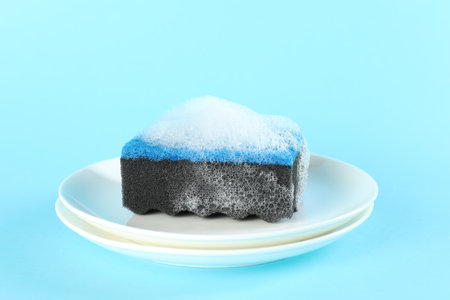 Sponge with foam and plates on light blue background, closeupの写真素材
