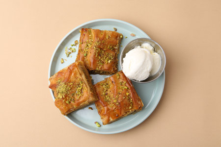 Baklava with crushed nuts and ice cream on beige table, top view