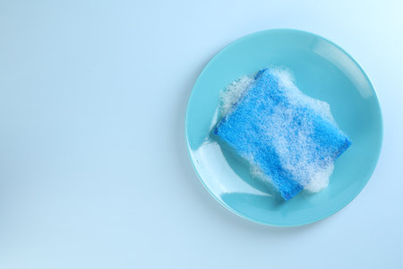 One sponge with foam and plate on light blue background, top view. Space for textの写真素材