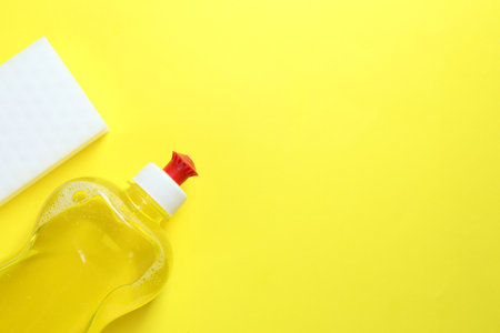 Sponge and bottle with detergent on yellow background, top view. Space for textの写真素材