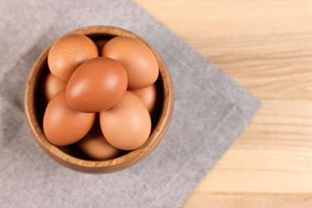 Raw eggs in bowl on wooden table, top view