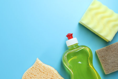 Different sponges and bottle with detergent on light blue background, flat lay. Space for textの写真素材