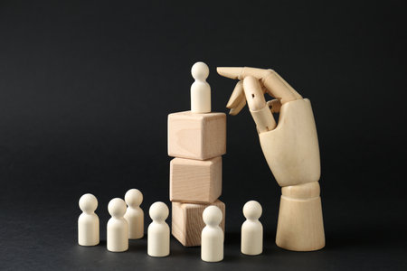 Competition concept. Human figure on wooden cubes, other ones behind and hand model against black backgroundの写真素材