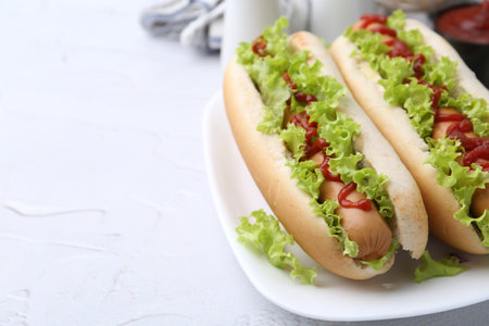 Tasty hot dogs with lettuce and ketchup on white table, closeup. Space for textの写真素材
