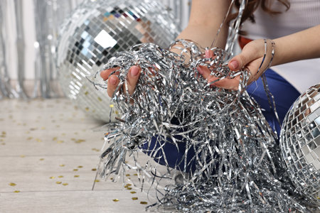 Woman with silver tinsel on floor indoors, closeup