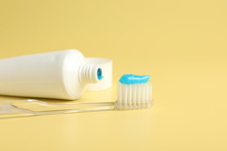 Toothbrush with toothpaste and tube on yellow background, closeup. Space for text