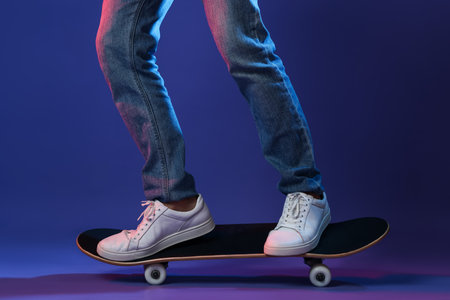 Man riding skateboard in color lights against blue background, closeupの写真素材