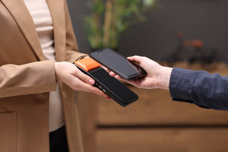 Woman paying with smartphone via terminal against blurred background, closeup