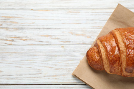 Paper bag with fresh croissant on wooden table, top view. Space for text